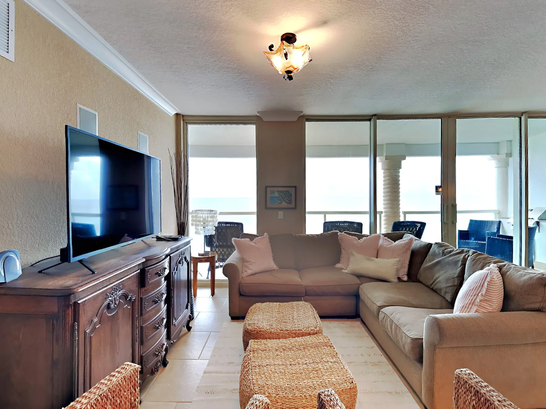 A living room with sectional seating, a television, and woven ottomans.