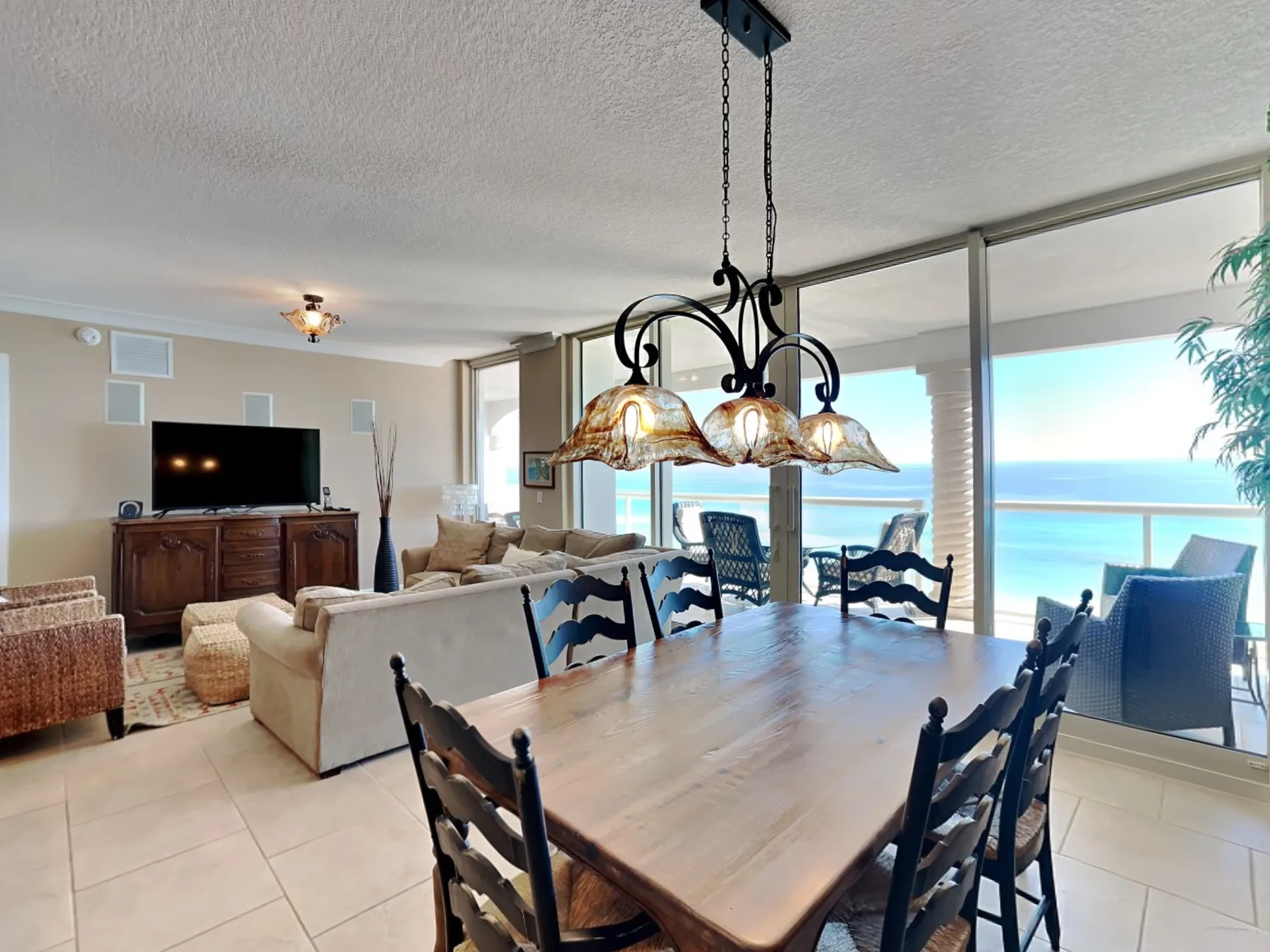 A dining area with a wooden table and seating beside large windows overlooking the ocean.