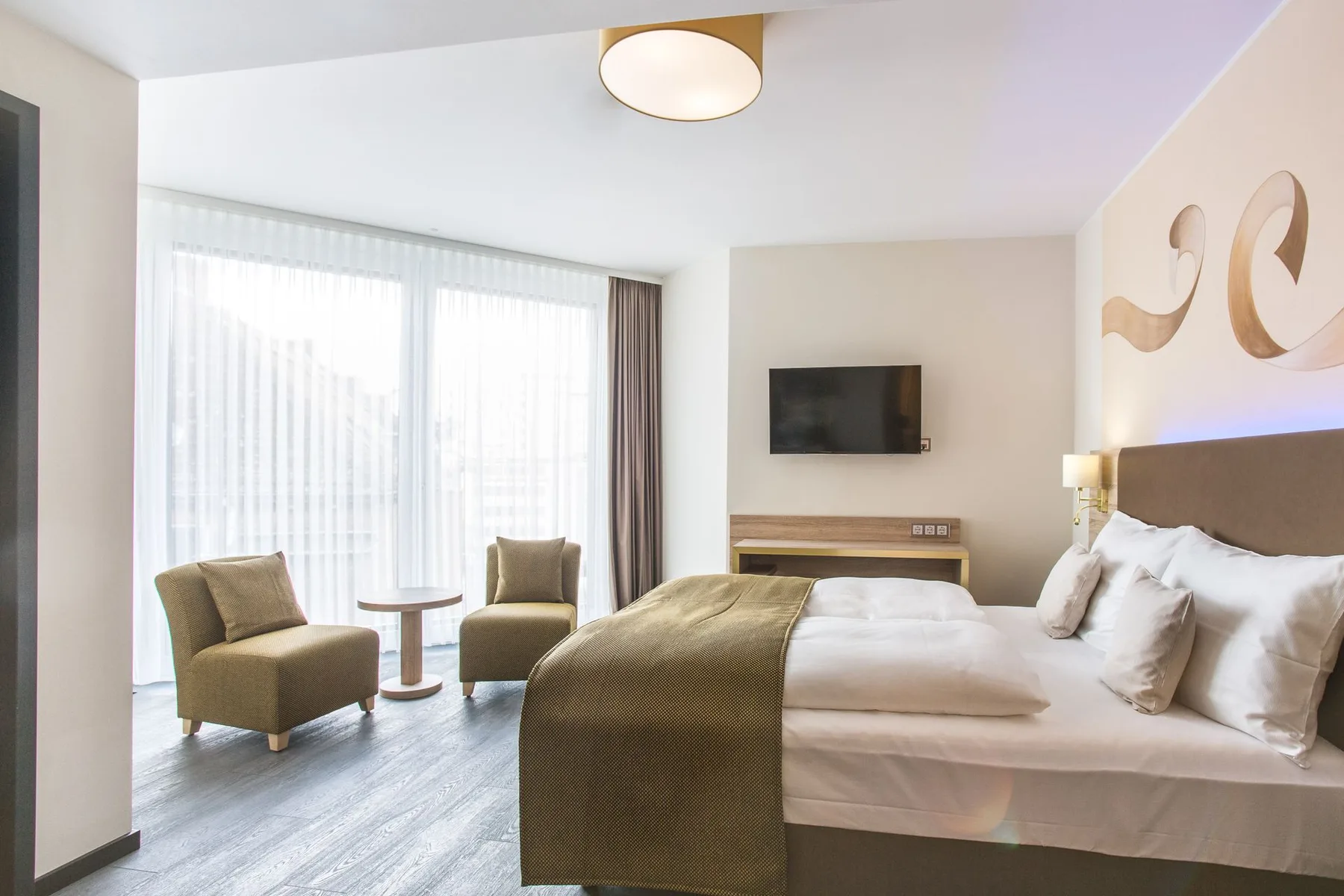 Habitación de hotel con una cama, sillas y una ventana grande.