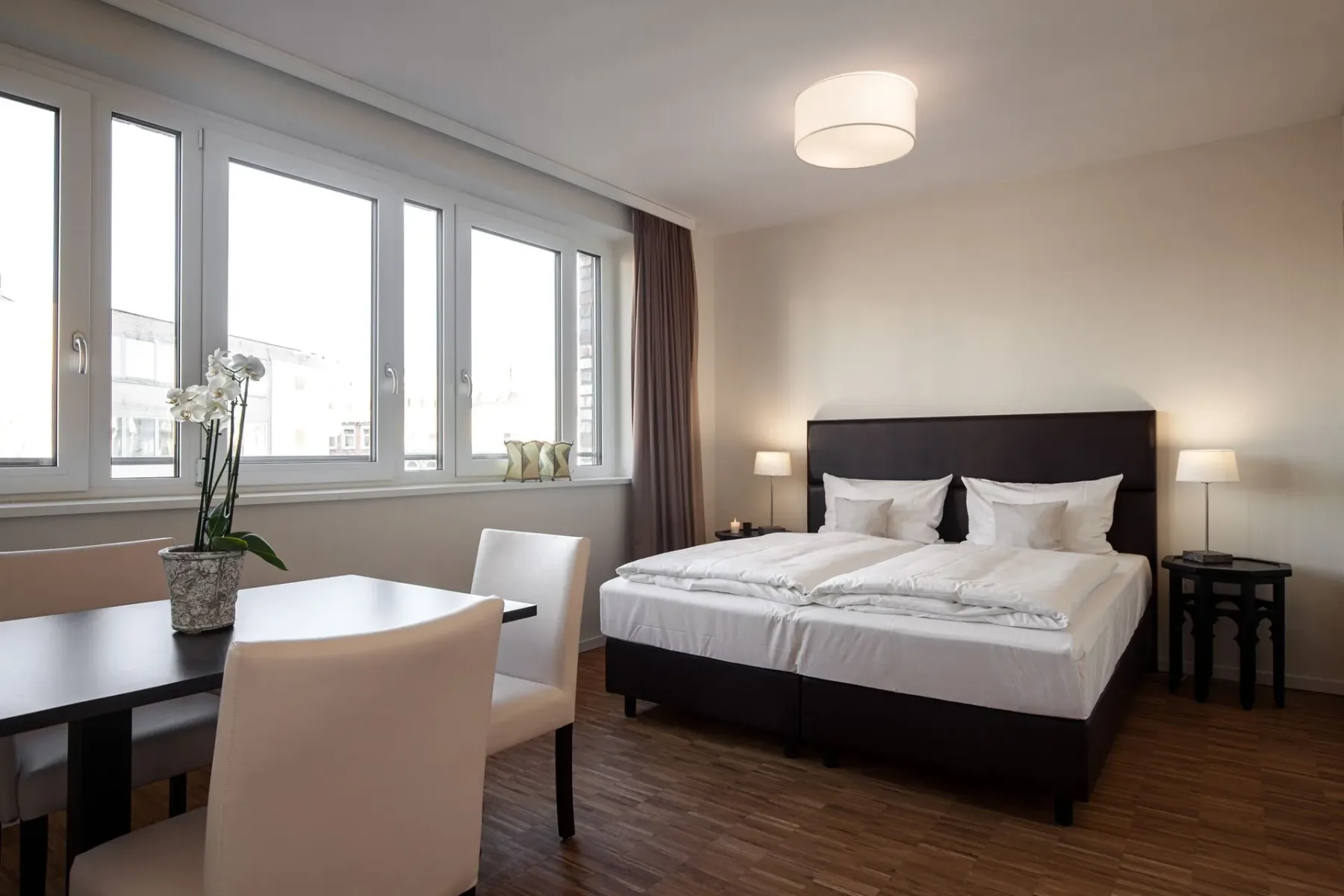 Dormitorio con una cama grande, una mesa de comedor y ventanas grandes.