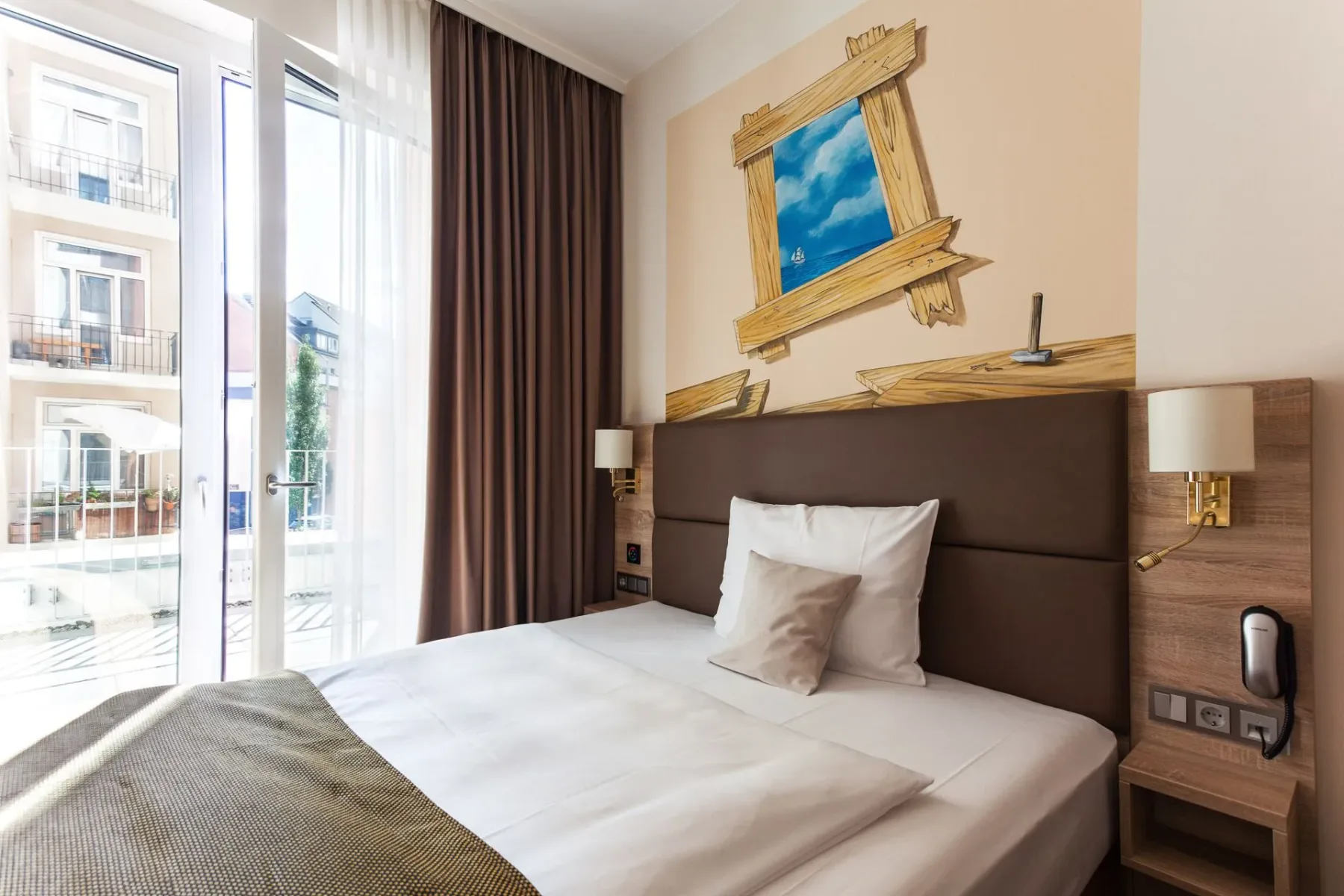 Habitación de hotel con una cama, una ventana grande y un mural ilustrado.