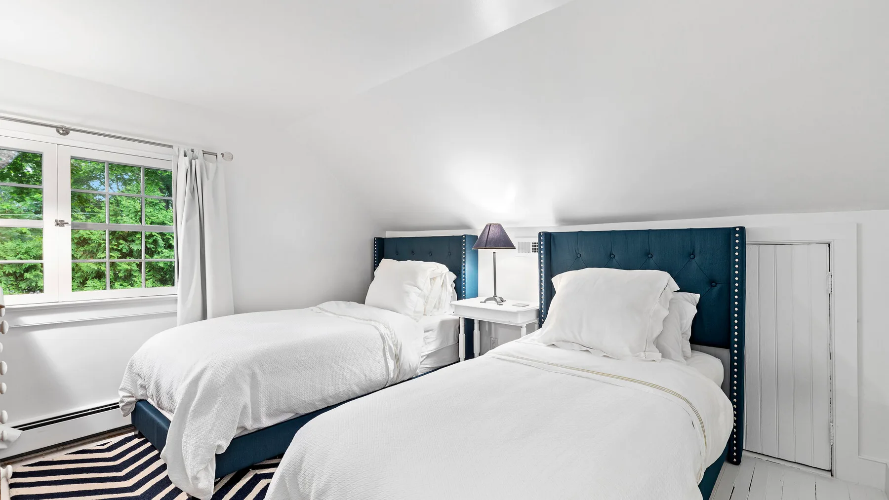 Un dormitorio luminoso con dos camas vestidas de blanco junto a una ventana.
