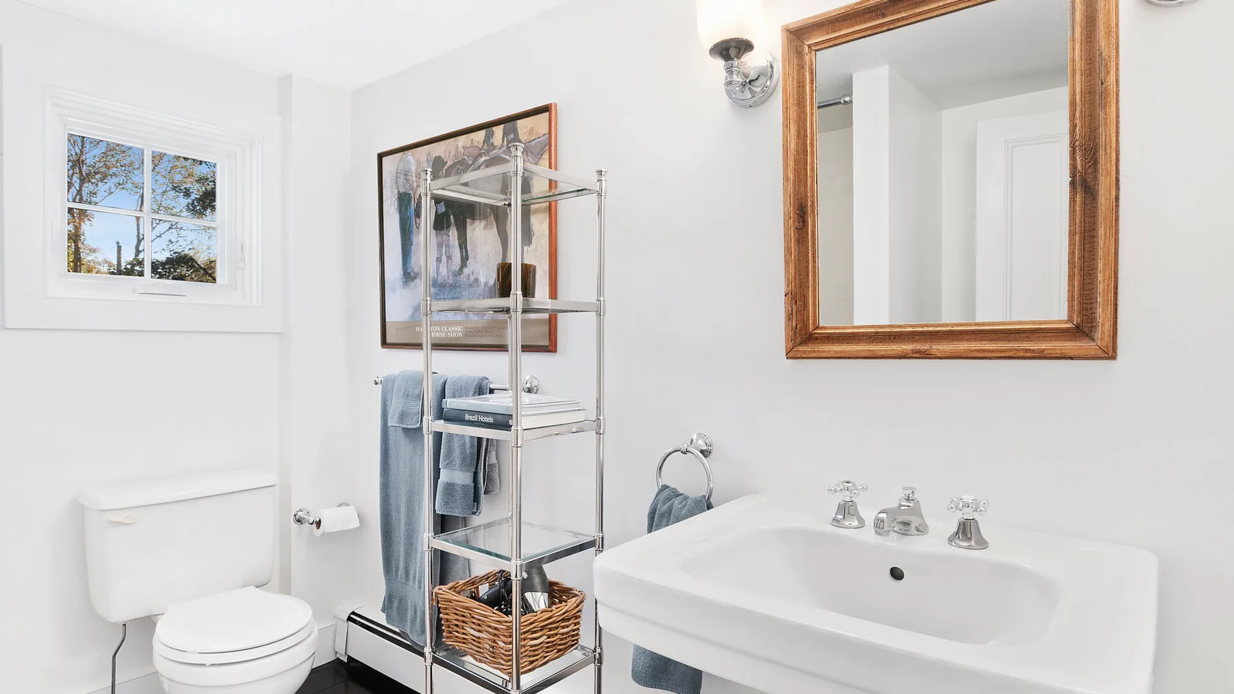 Un baño luminoso con lavabo, inodoro y estantería metálica.
