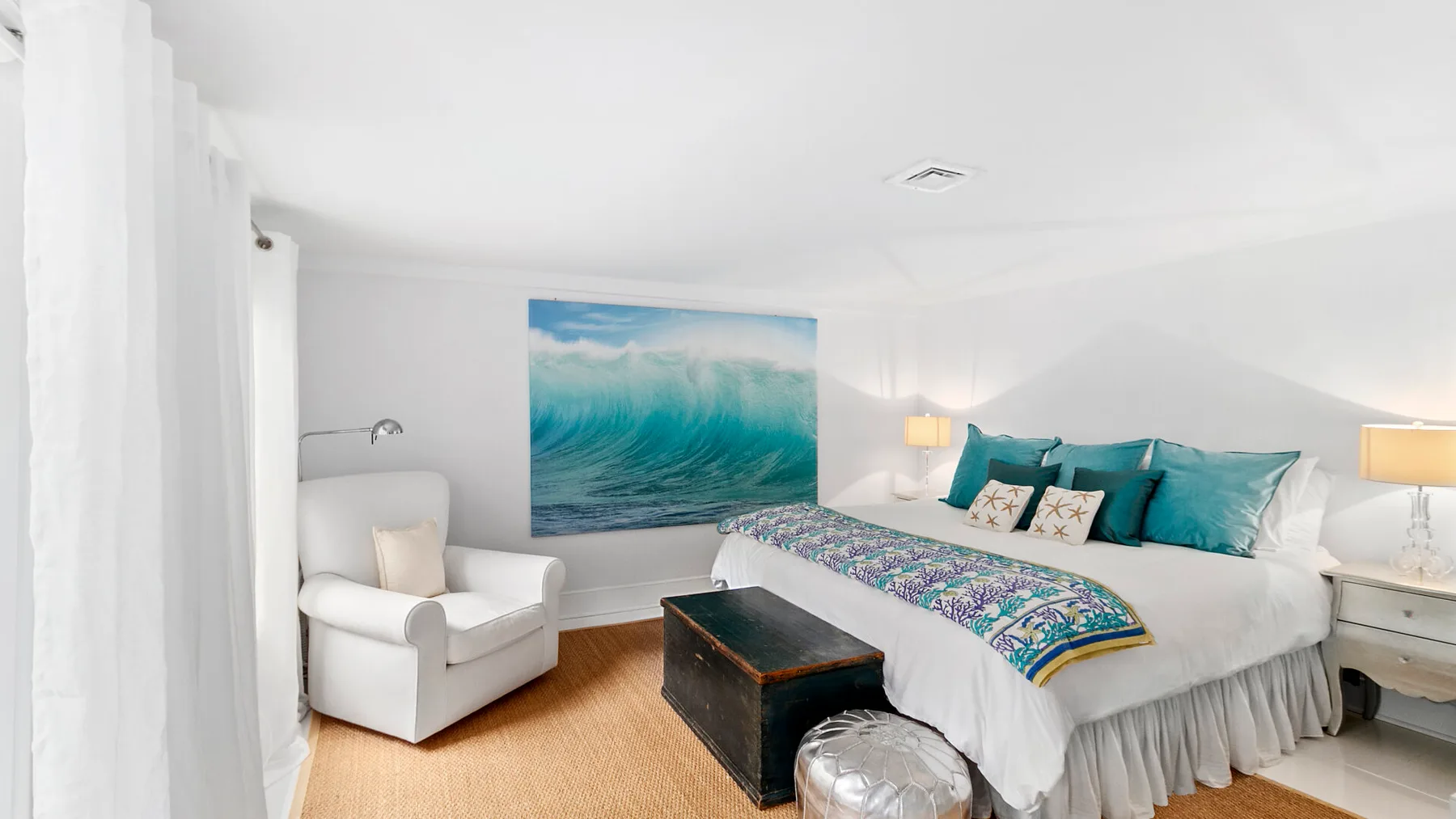 Un dormitorio luminoso con una cama grande, almohadas turquesas y un sillón.