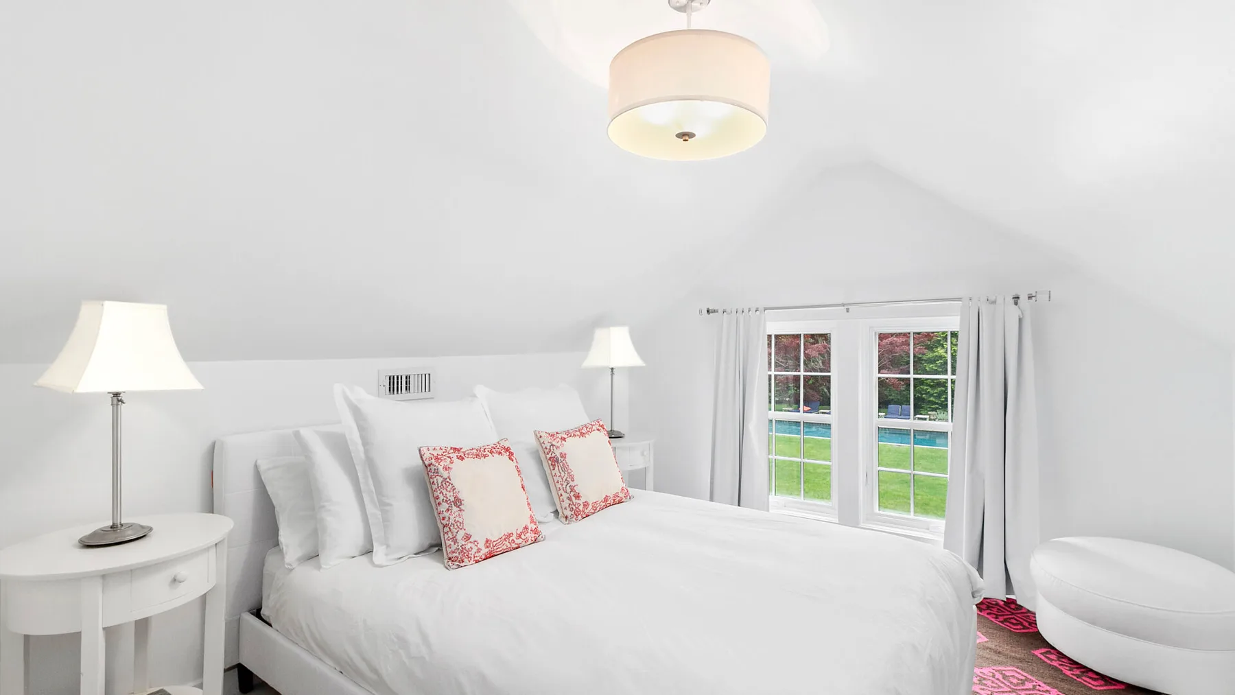 Un dormitorio luminoso con una cama bien tendida junto a ventanas con vistas a zonas verdes.