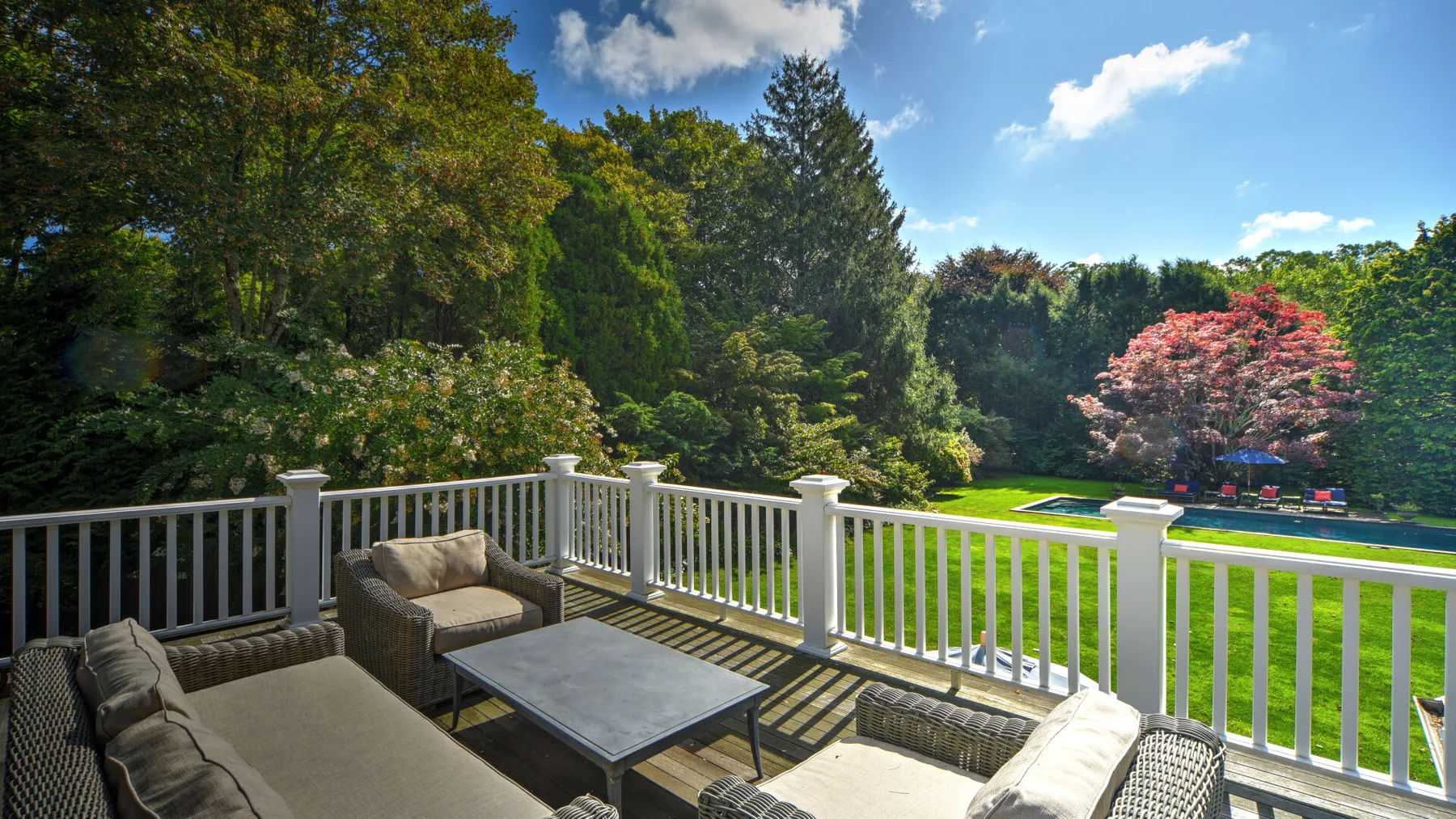 A furnished outdoor deck overlooks a green lawn and surrounding trees.