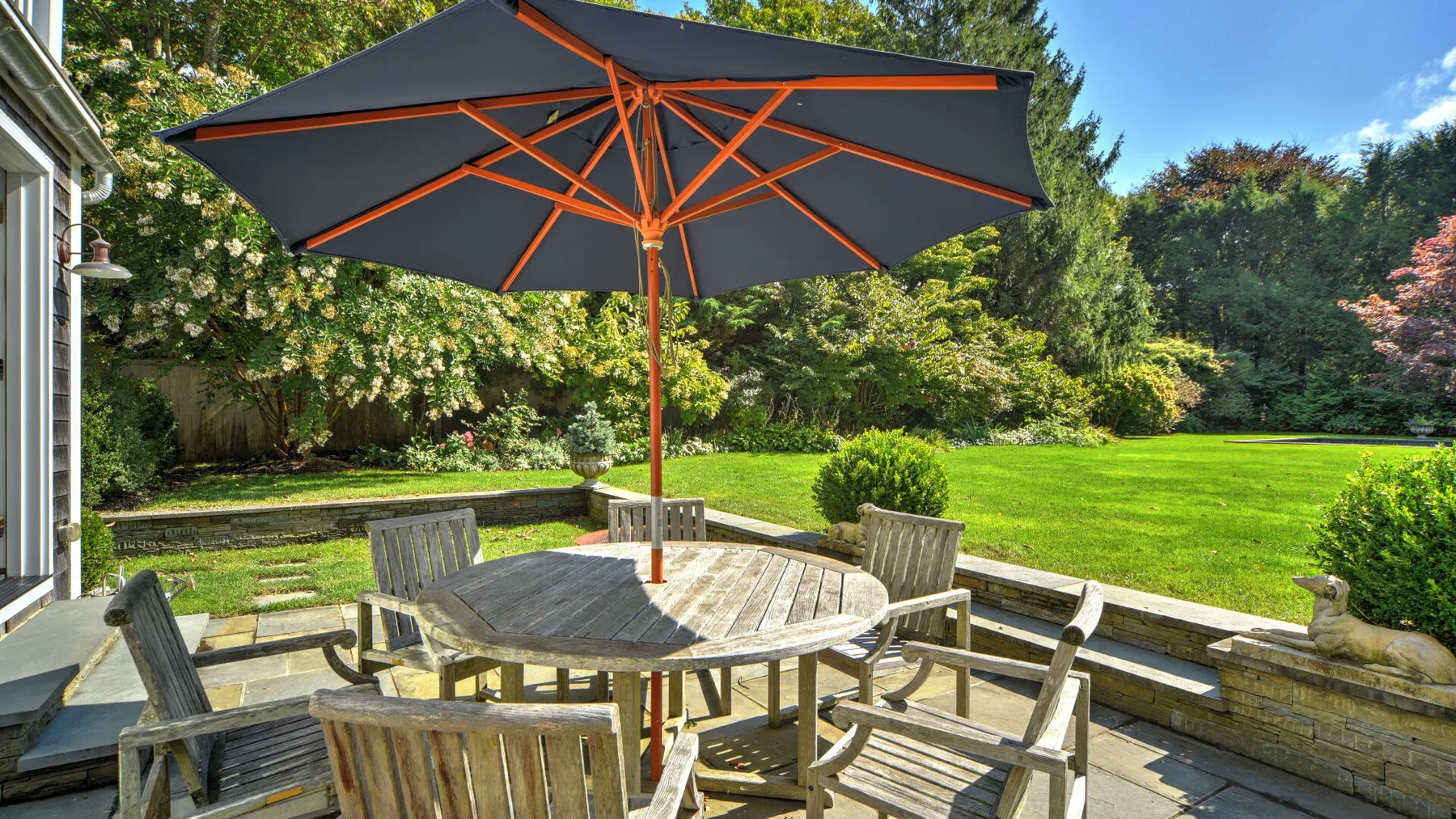 A patio dining area sits beneath a large umbrella beside a green lawn.