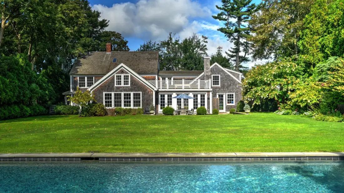 A large house overlooks a swimming pool and broad green lawn.