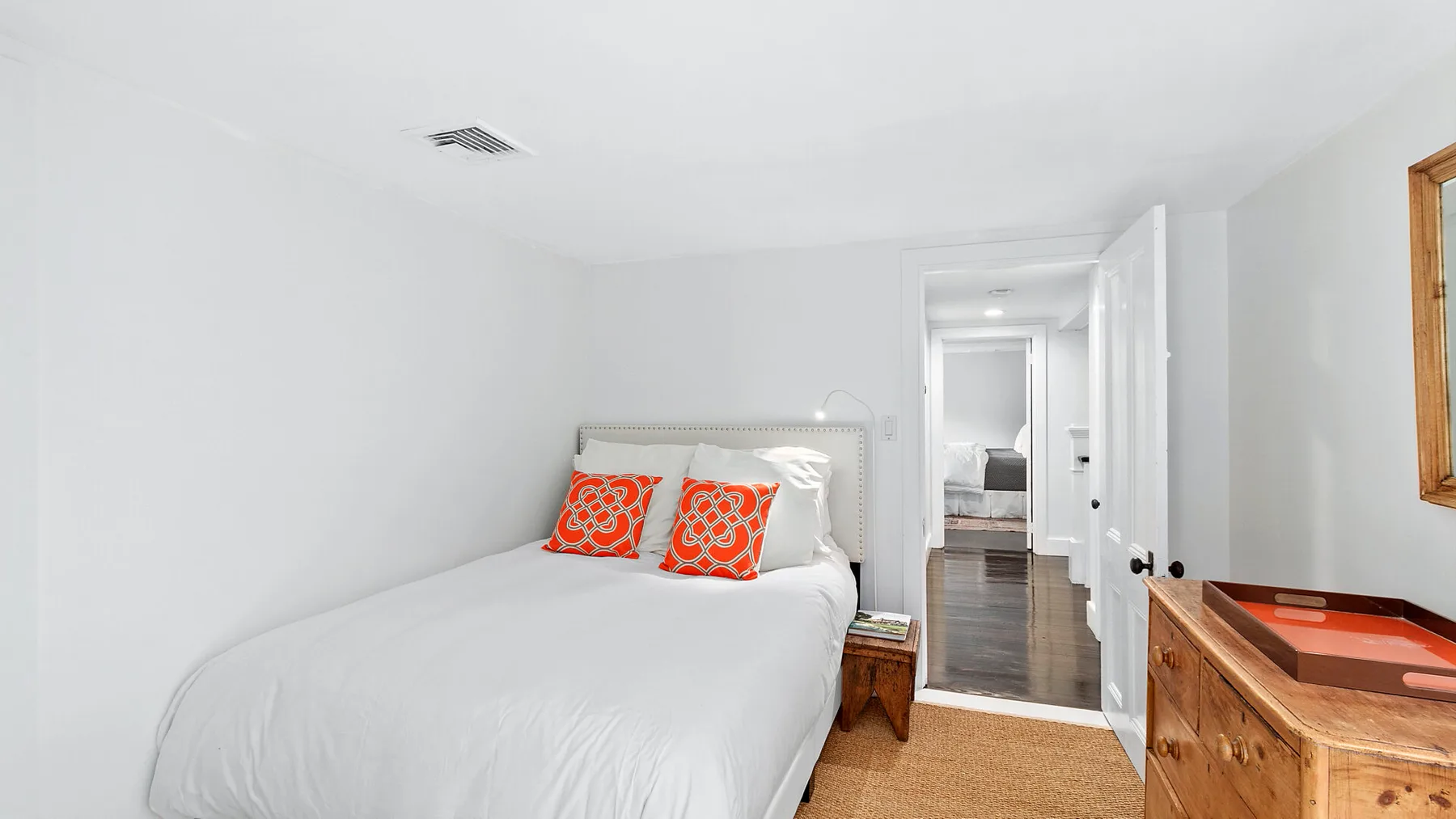 Un dormitorio luminoso con una cama vestida de blanco y una cómoda de madera.