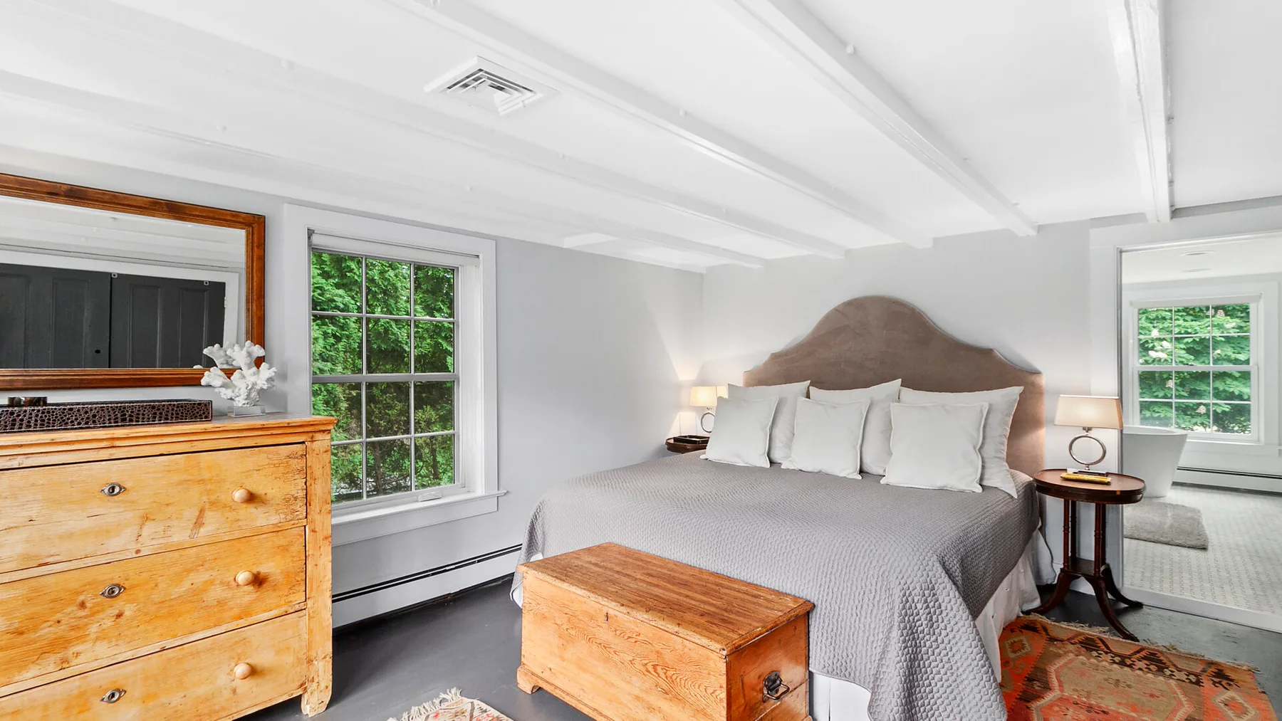 Dormitorio con una cama grande, una cómoda de madera y ventanas.