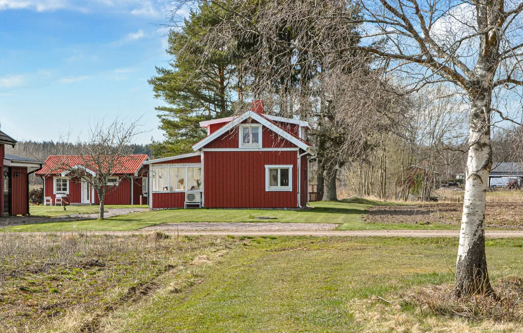 Red wooden buildings stand beside a grassy lawn and leafless trees.