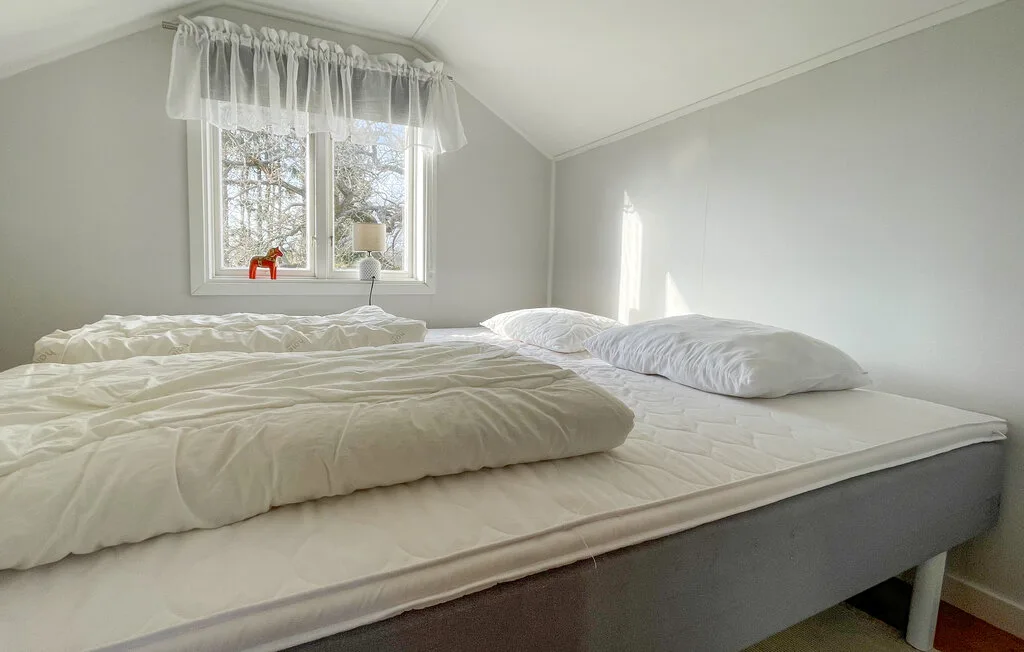 A bright bedroom with a bed beneath a window with sheer curtains.