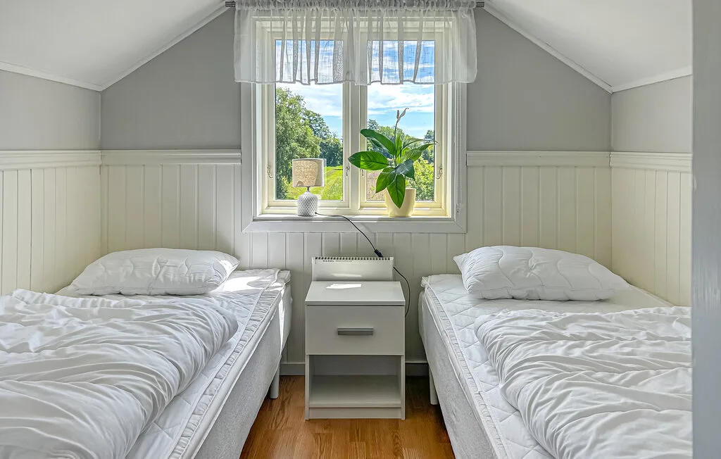 A bright bedroom with two beds, a nightstand, and a window.