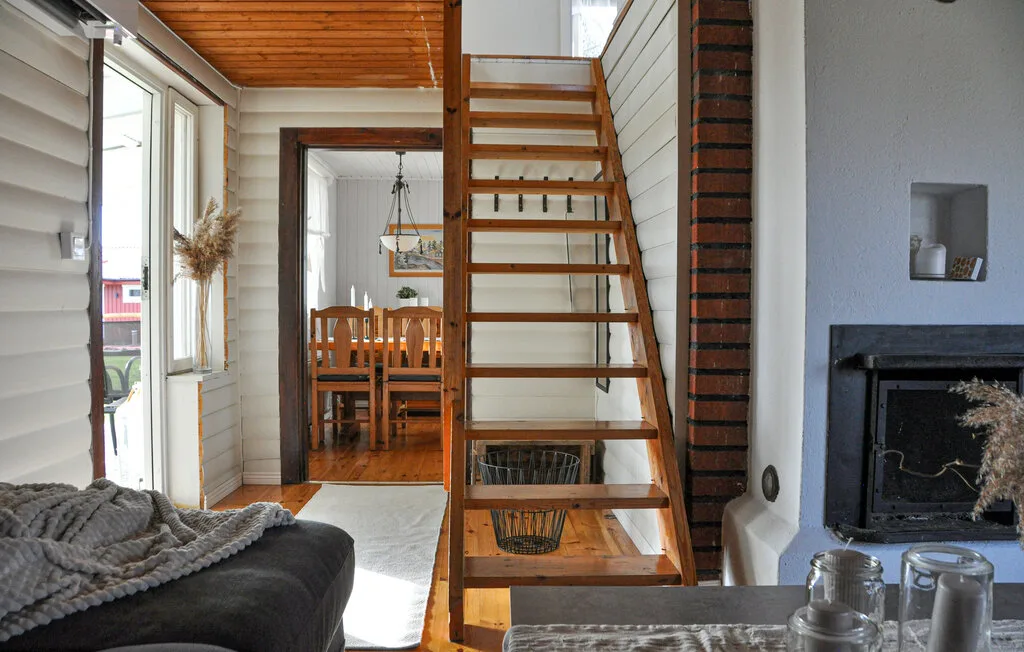A bright living area with a wooden staircase and dining table beyond.