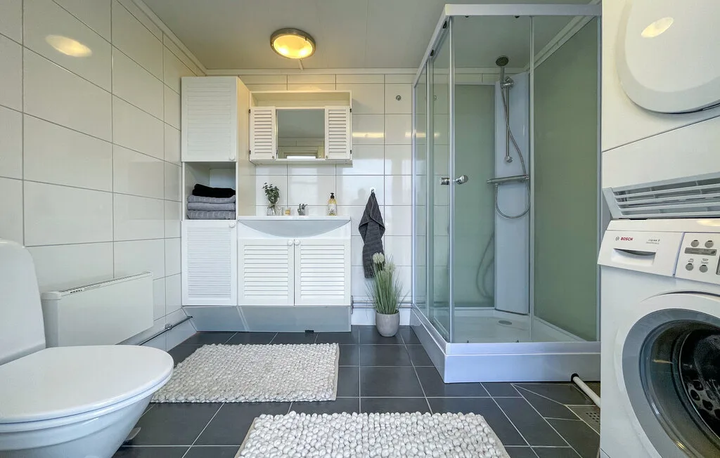 A tiled bathroom with a glass shower, sink, toilet, and washing machine.