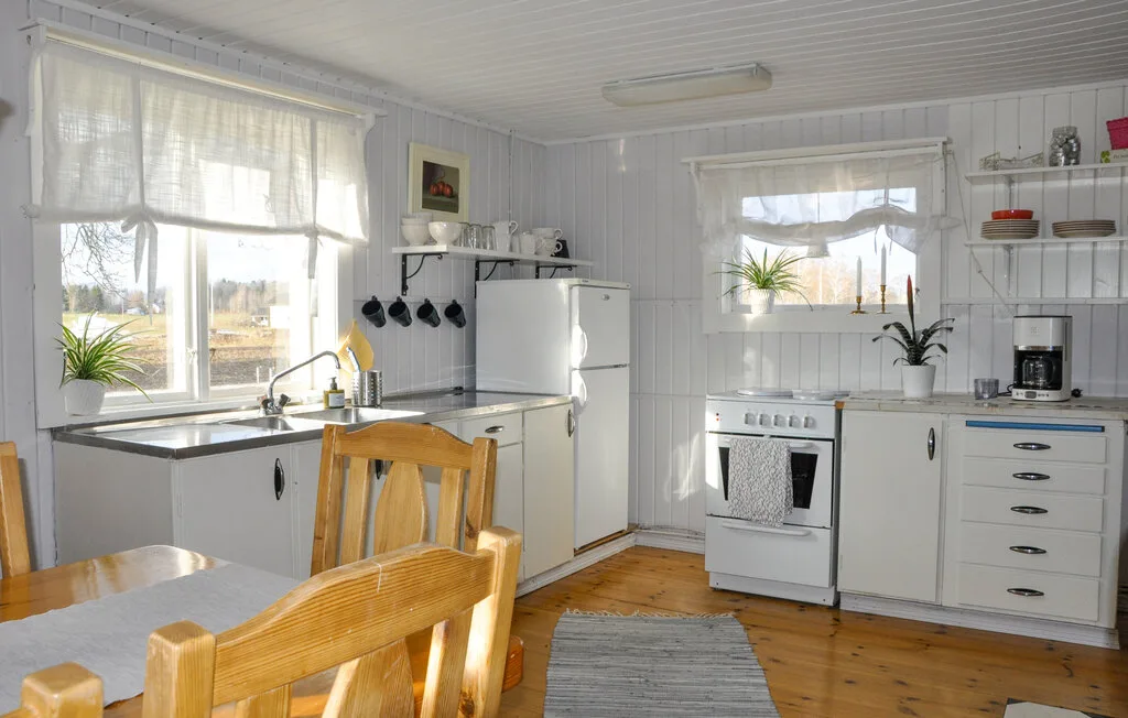 Una cocina luminosa con armarios blancos, una mesa de comedor y ventanas grandes.