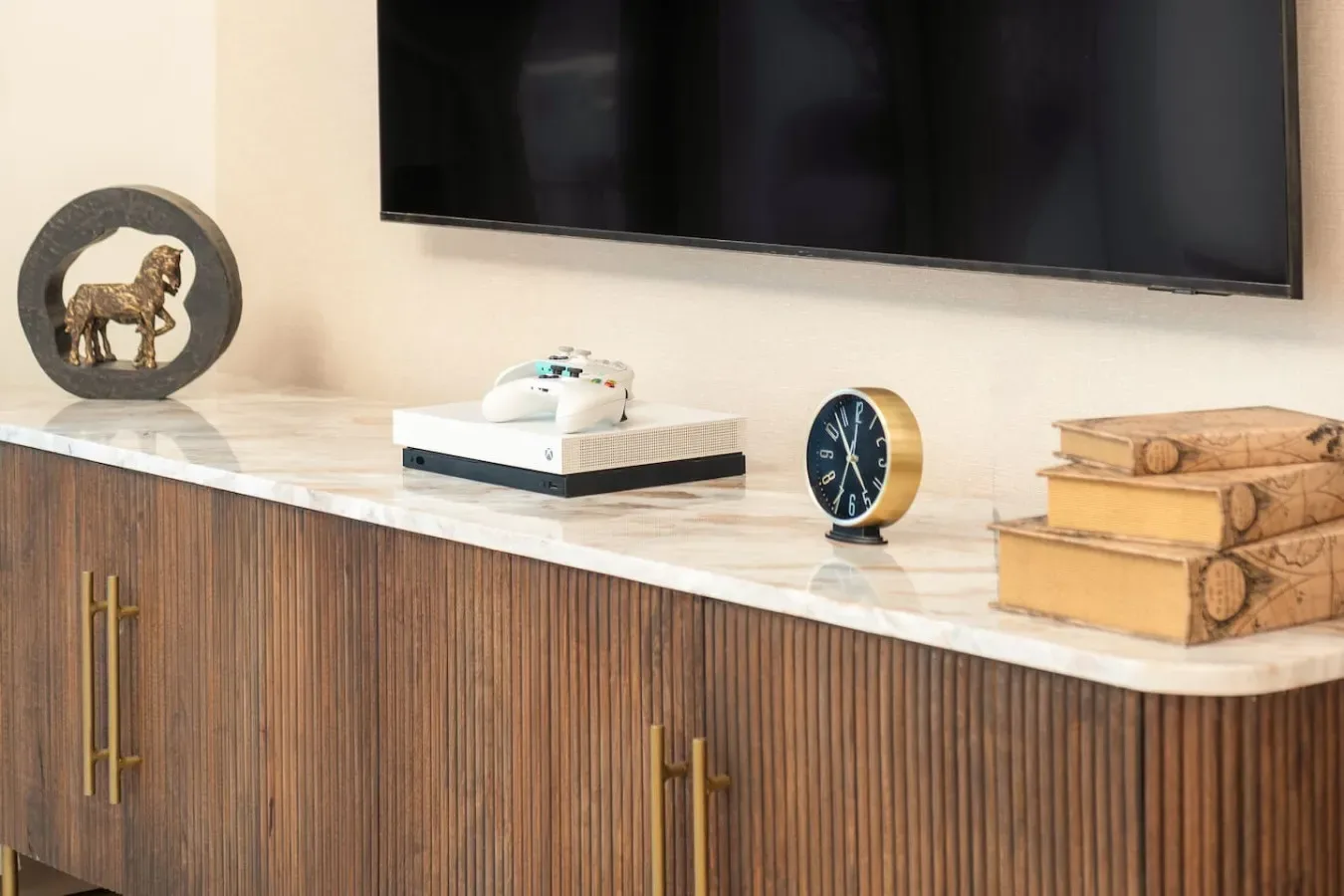 A living room console beneath a wall-mounted television, decorated with a clock and books.