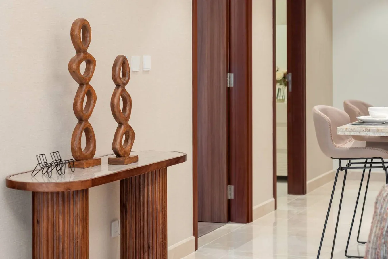 A hallway console table displays wooden sculptures beside a dining area.