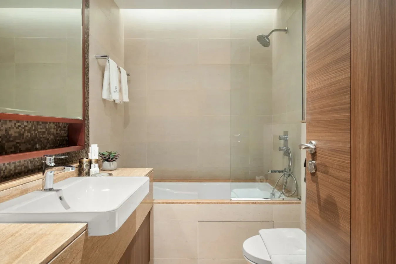 A bathroom with a sink and a bathtub behind a glass partition.