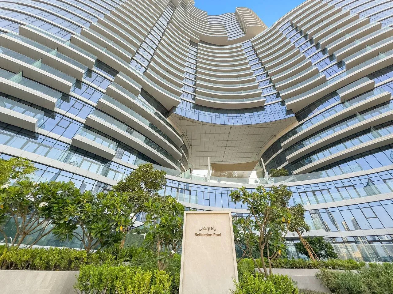 A modern high-rise building rises above landscaped greenery beneath a clear sky.