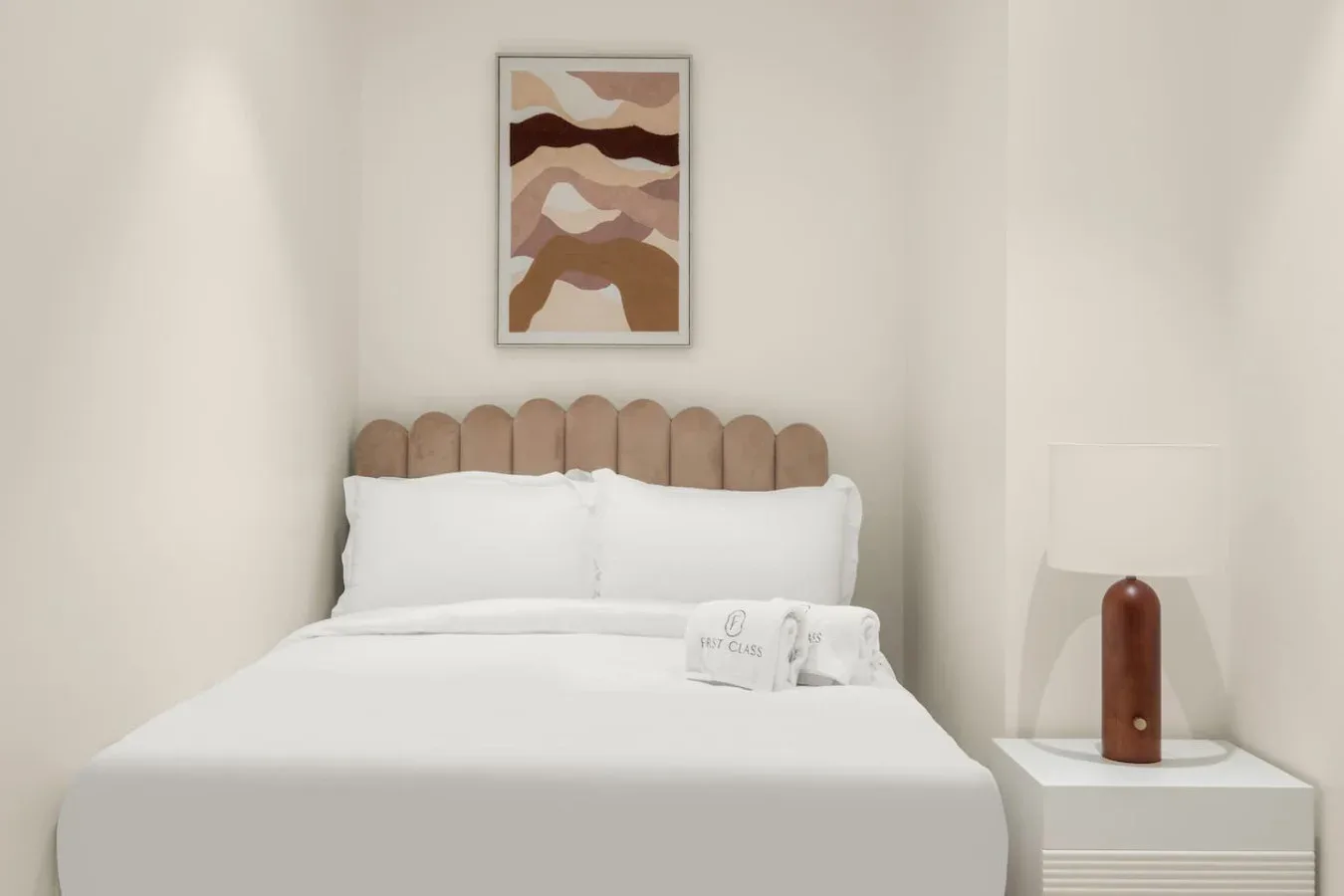 A neatly made bed sits beneath abstract landscape artwork in a bright bedroom.