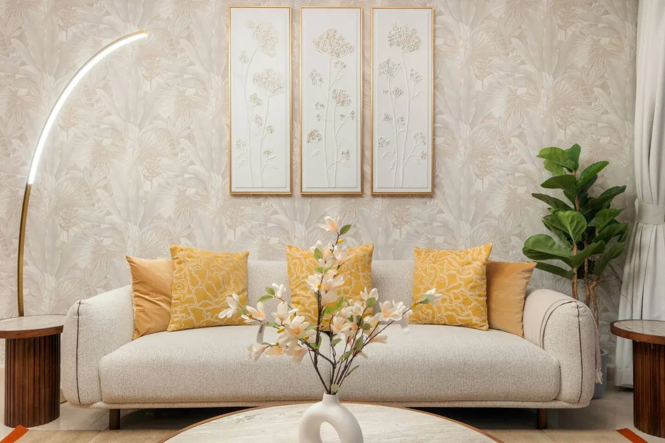 A bright living room features a cream sofa with yellow cushions and framed floral art.
