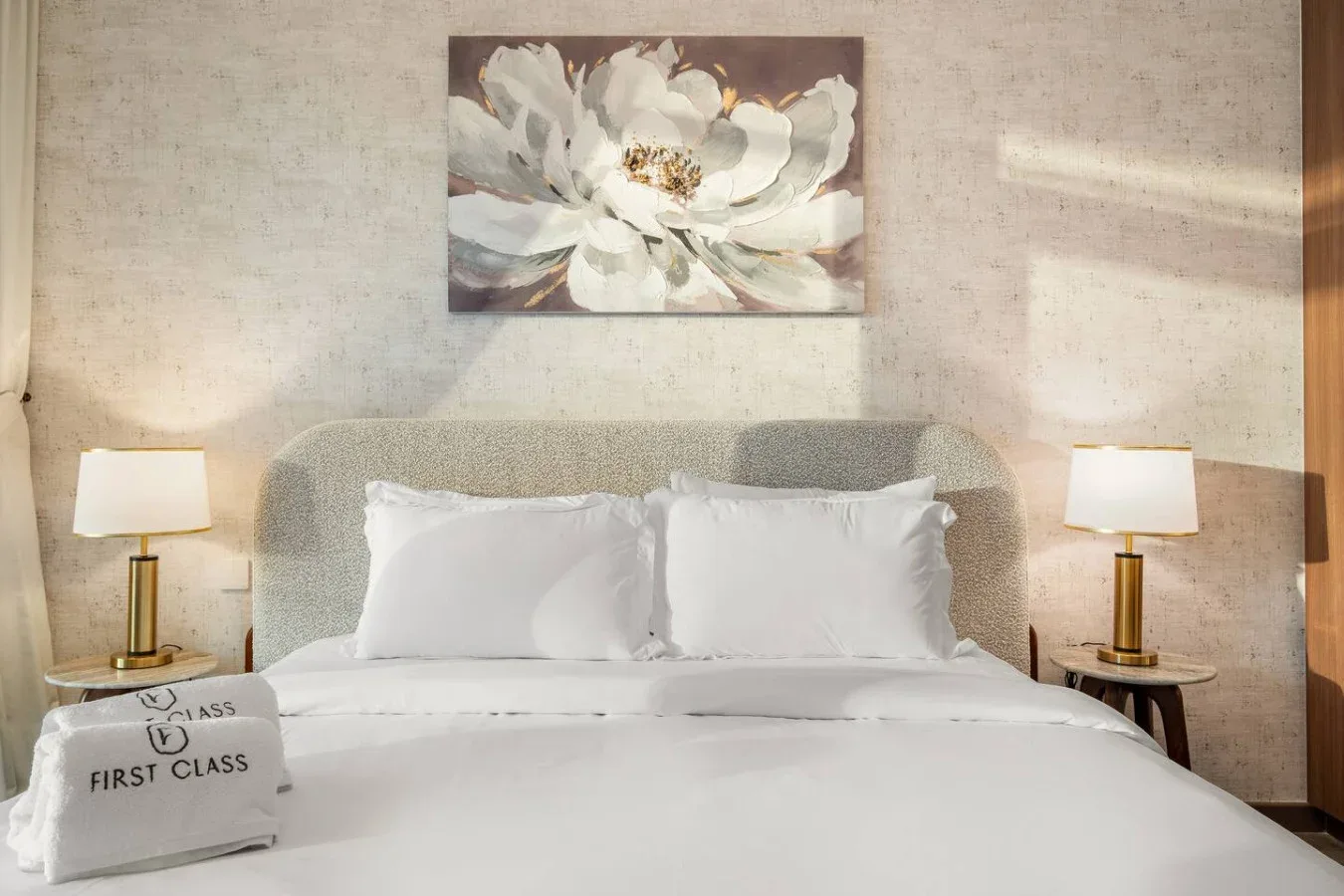 A bedroom with a neatly made bed, matching bedside lamps, and floral wall art.