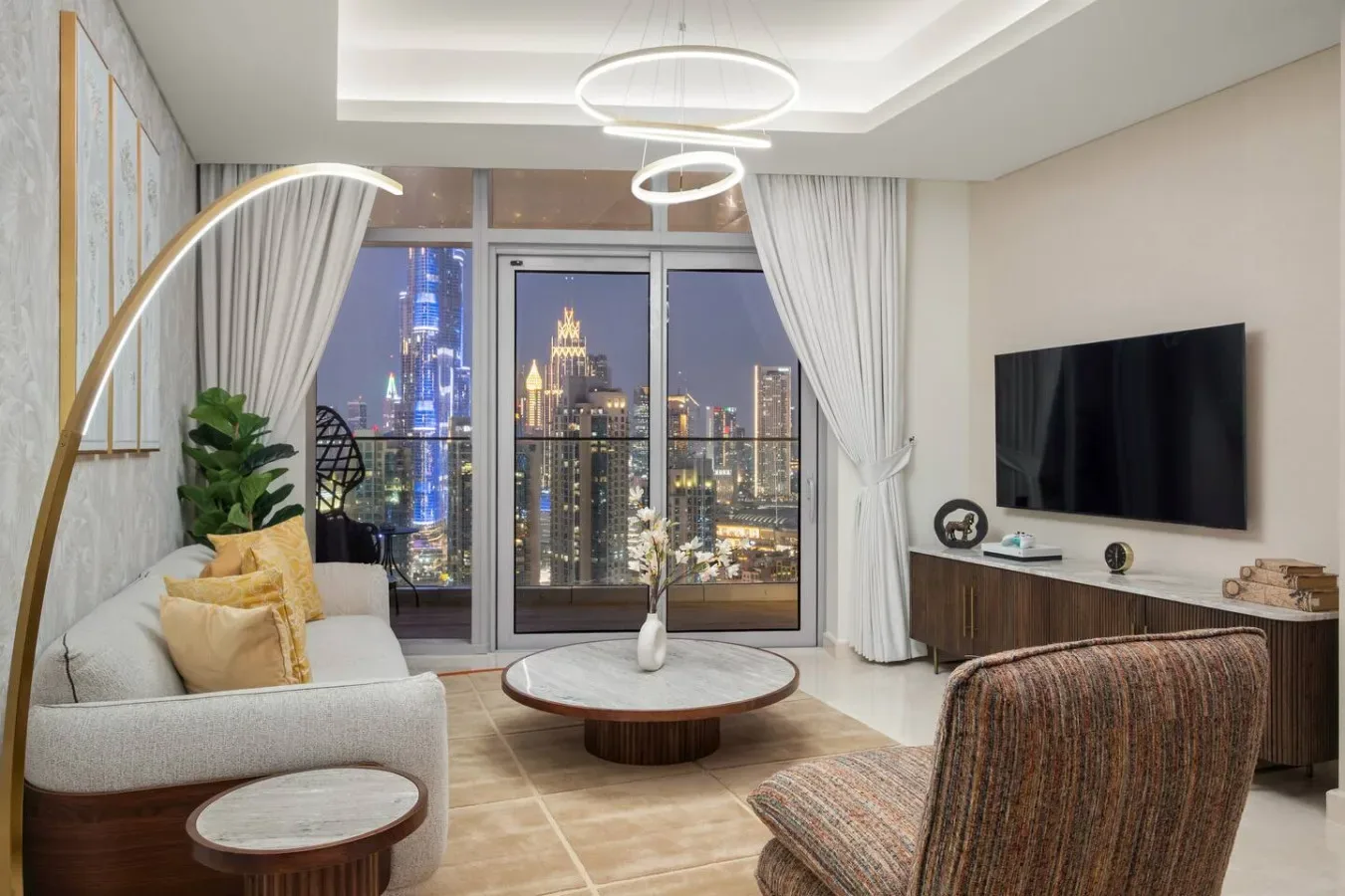 A modern living room with seating, a television, and a city view through large windows.