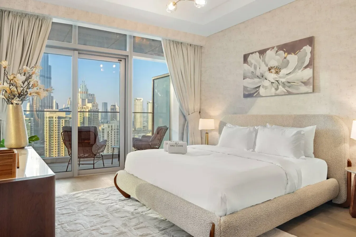 A bright bedroom with a large bed and floor-to-ceiling windows overlooking city buildings.