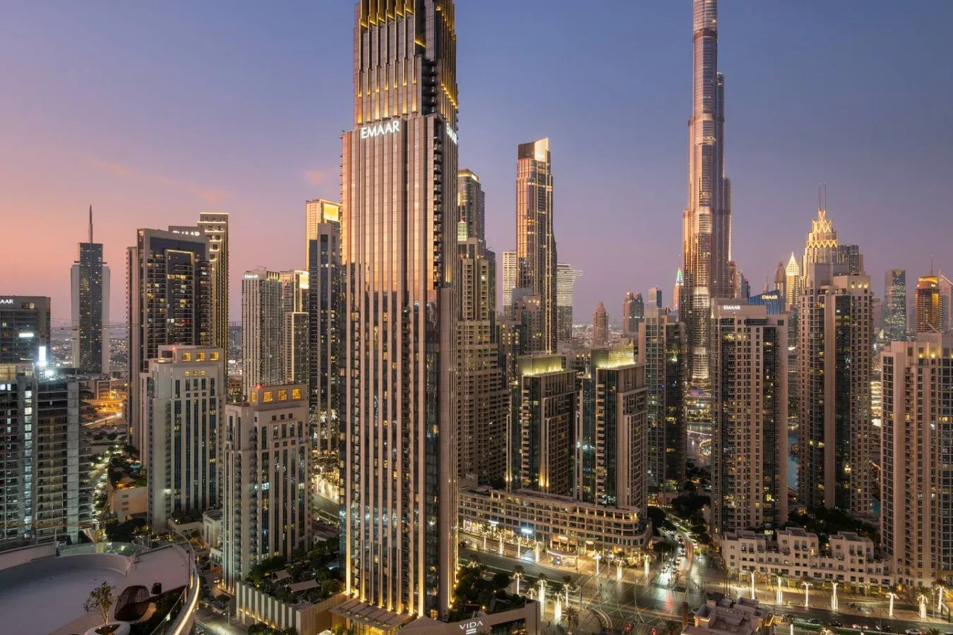 A city skyline at dusk, with illuminated skyscrapers rising above the surrounding buildings.