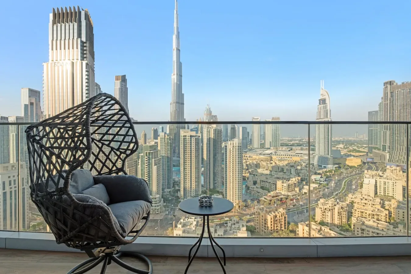 A balcony seating area overlooks a city skyline through a glass railing.