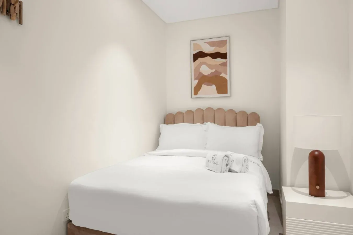 A bedroom with a neatly made bed and abstract artwork above the headboard.