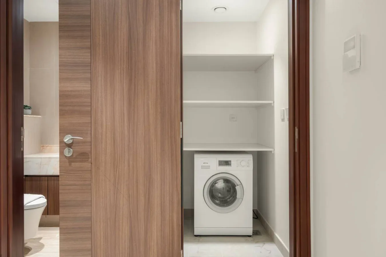 A laundry area with a front-loading washing machine beneath open shelves.