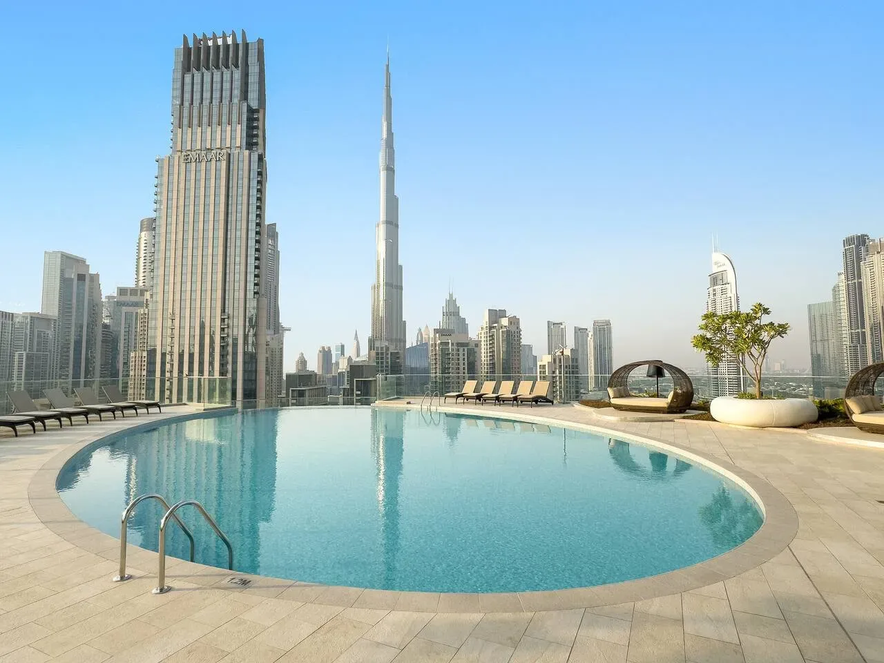 A rooftop swimming pool overlooks a city skyline, with lounge seating along the deck.