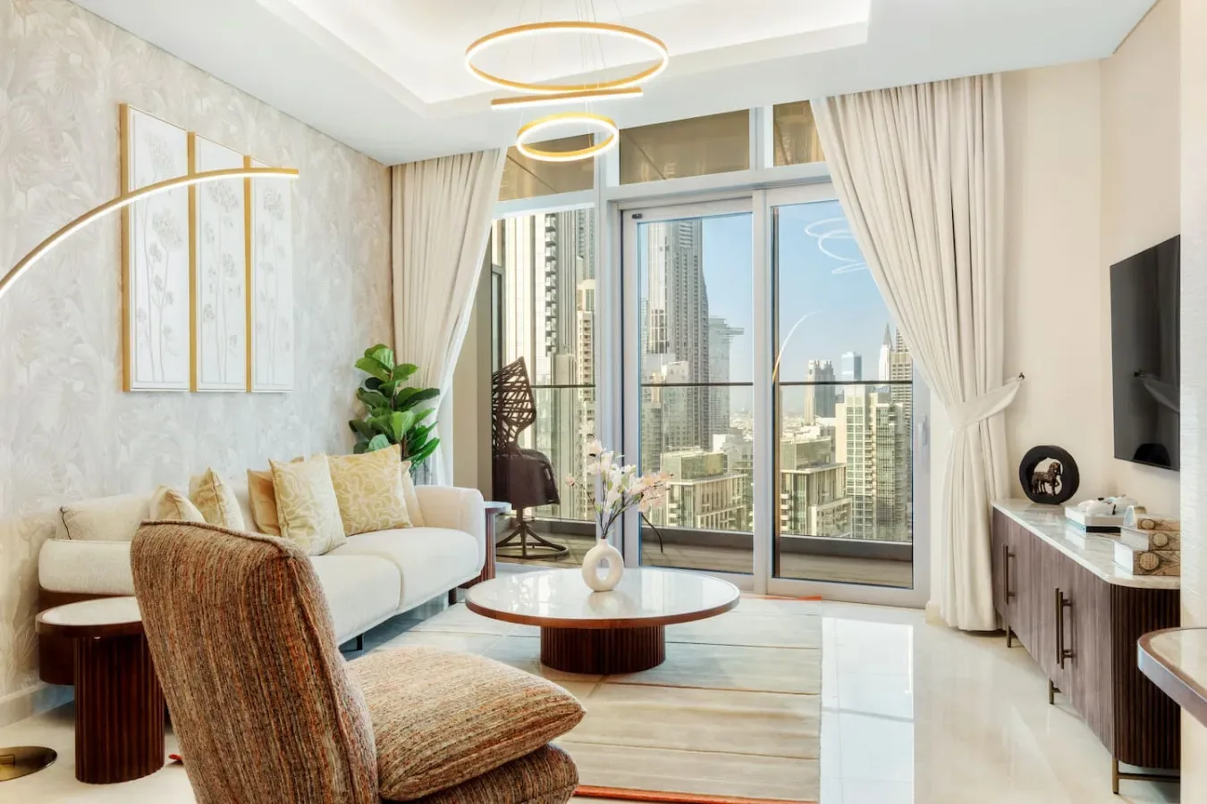 A bright living room with seating, a coffee table, and large windows overlooking city buildings.