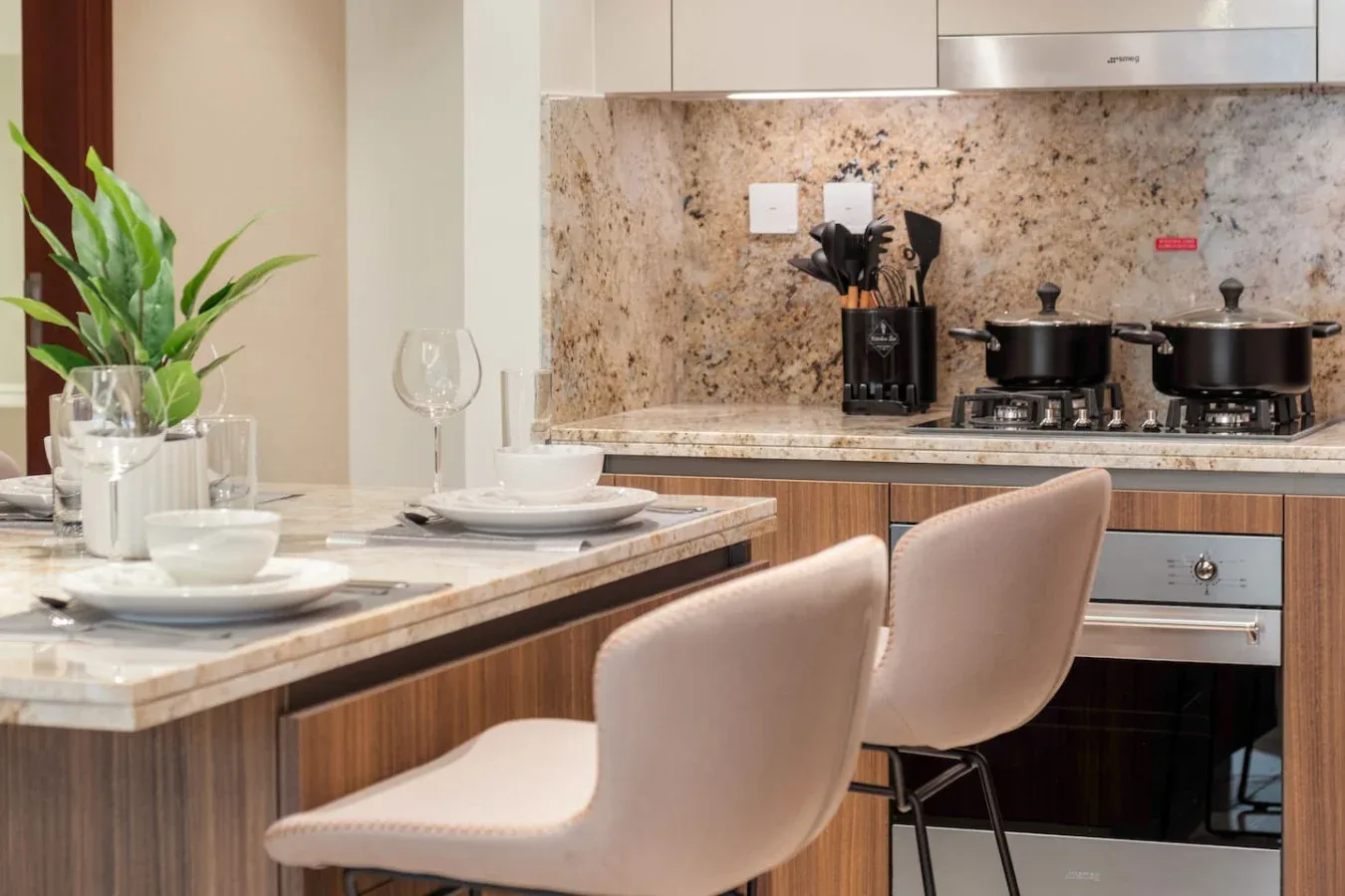 A kitchen counter with place settings sits beside a stovetop and cookware.
