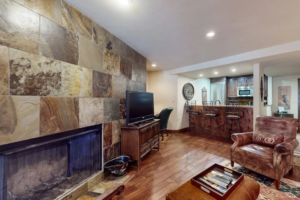 Una sala de estar con chimenea de piedra, televisor y asientos junto a una barra de cocina.