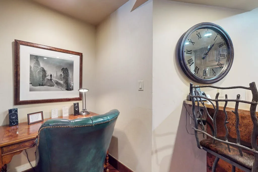 Un escritorio y una silla están bajo una obra enmarcada, junto a un gran reloj de pared.