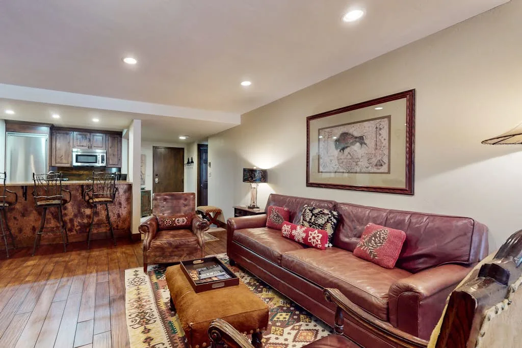 A living room with leather seating, a coffee table, and an open kitchen area.