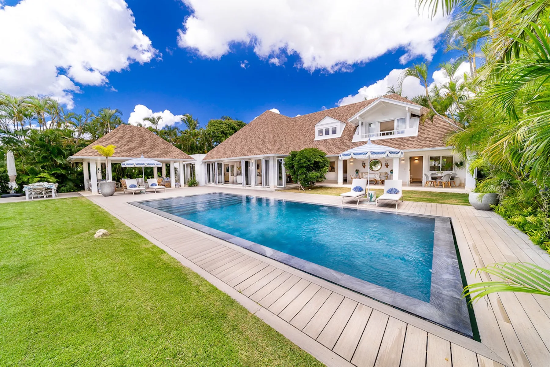 Una amplia piscina exterior está junto a una casa espaciosa y un césped verde.