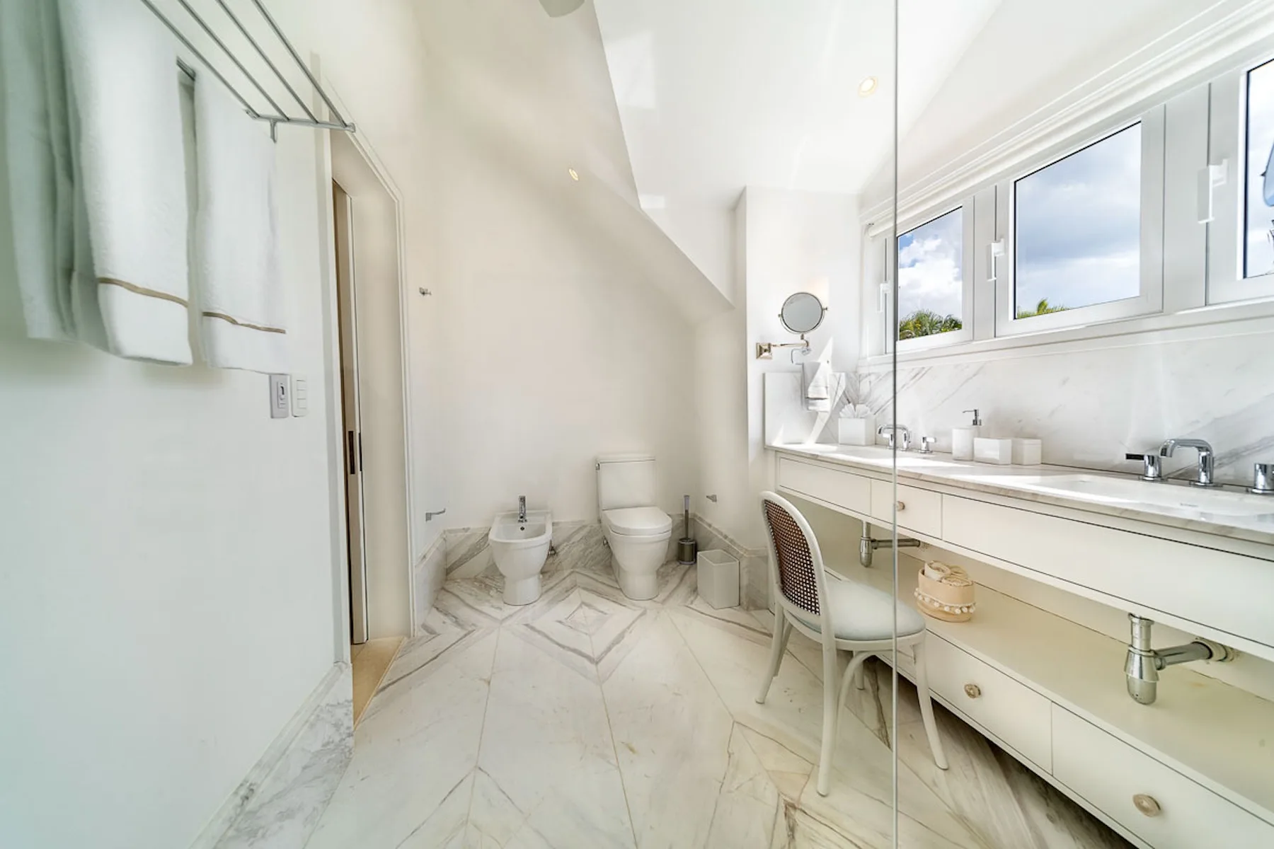 Un baño luminoso con un tocador largo bajo amplias ventanas.