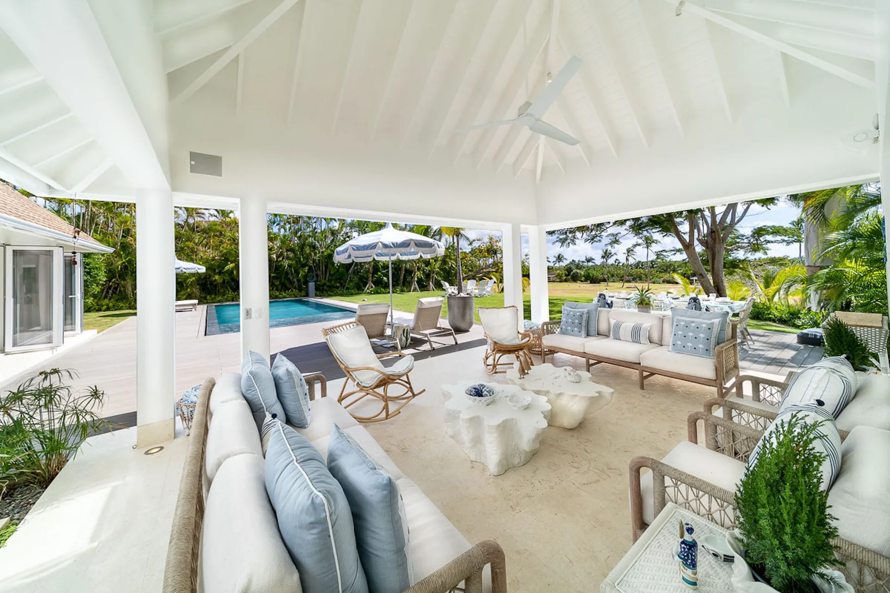 Una zona de estar exterior cubierta da a una piscina y un jardín.