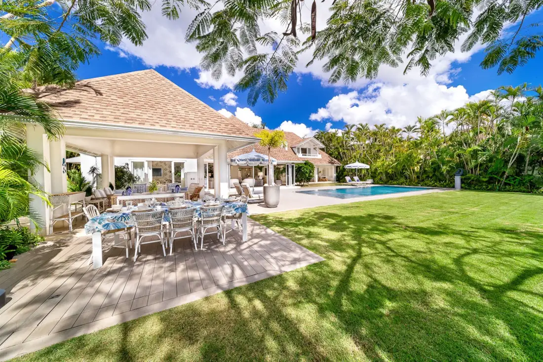 Un patio al aire libre con asientos para comer da a un césped y una piscina.