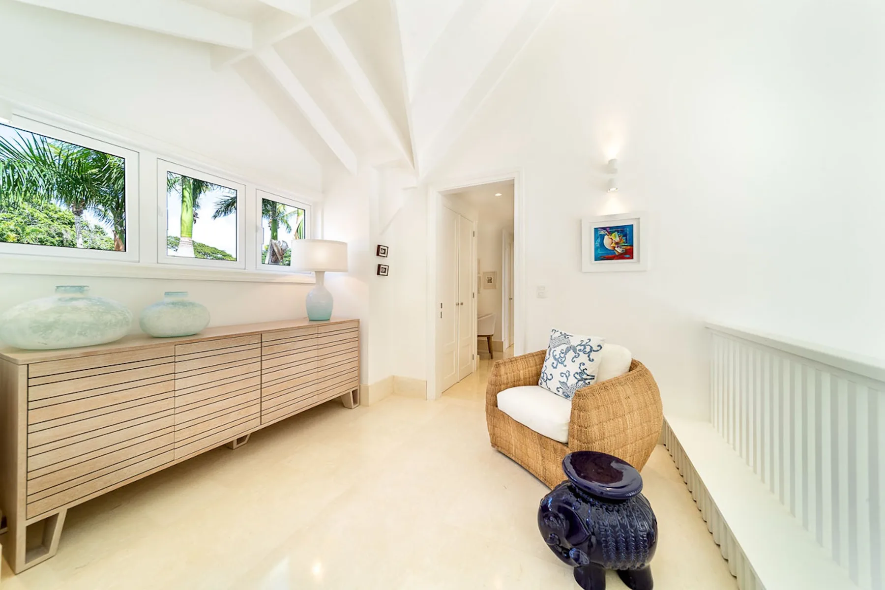 Sala de estar luminosa con asiento tejido y un mueble largo de madera bajo las ventanas.