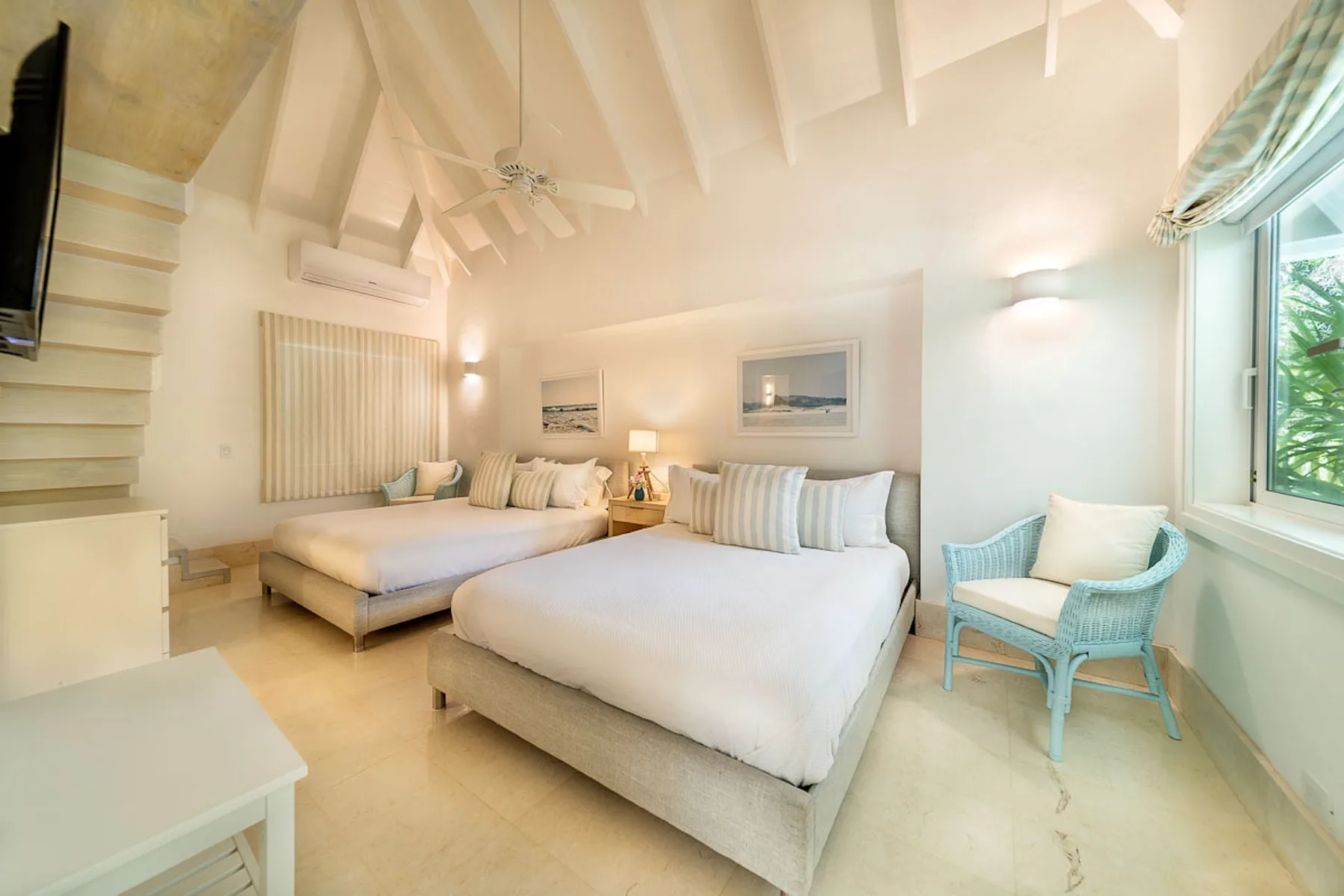 Un dormitorio luminoso con dos camas y una silla azul junto a la ventana.