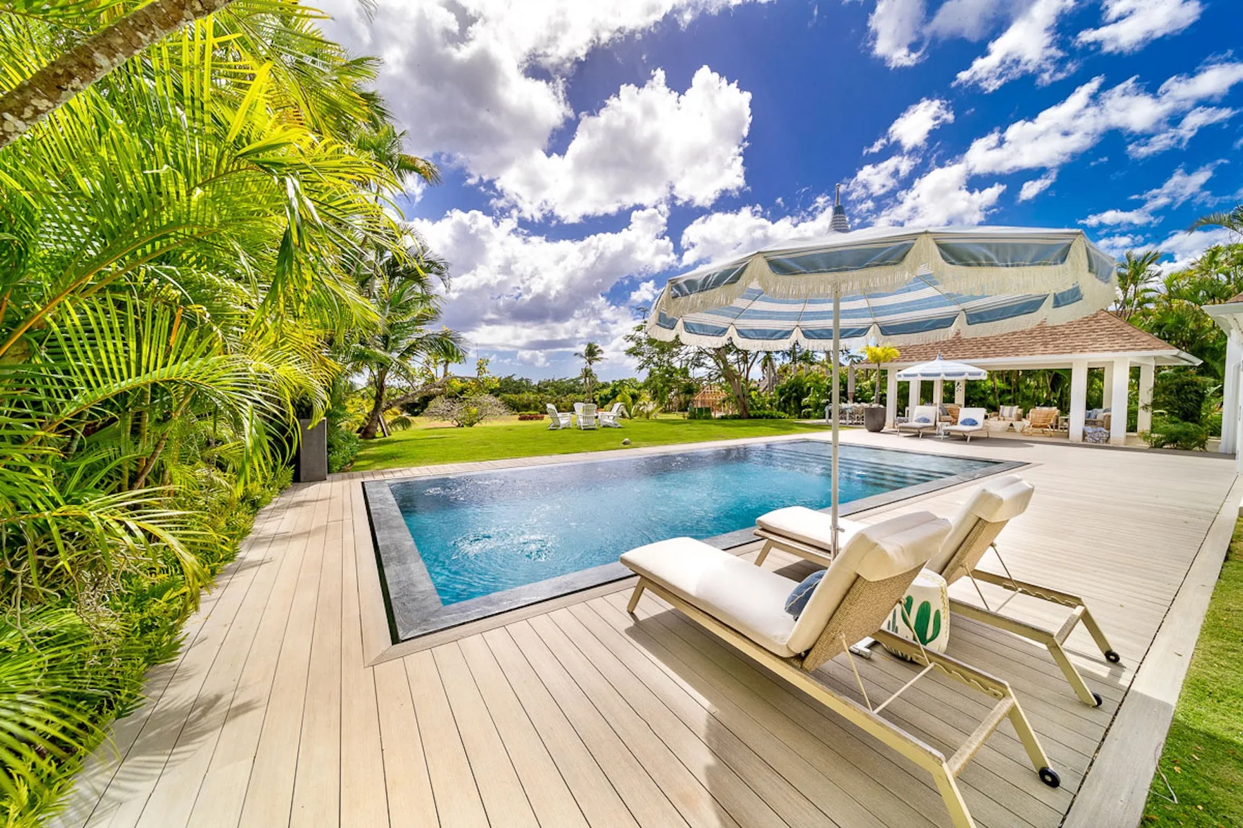 Una piscina exterior junto a una terraza de madera con asientos reclinables.