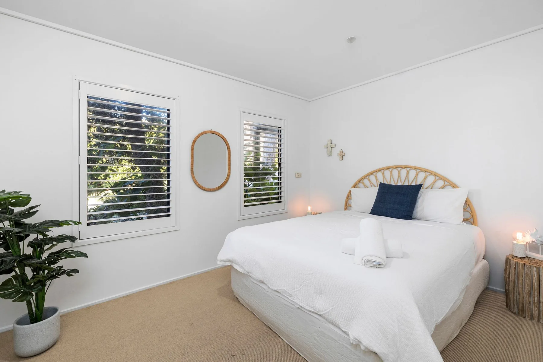Un dormitorio luminoso con una cama bien tendida y ventanas que dan a la vegetación.