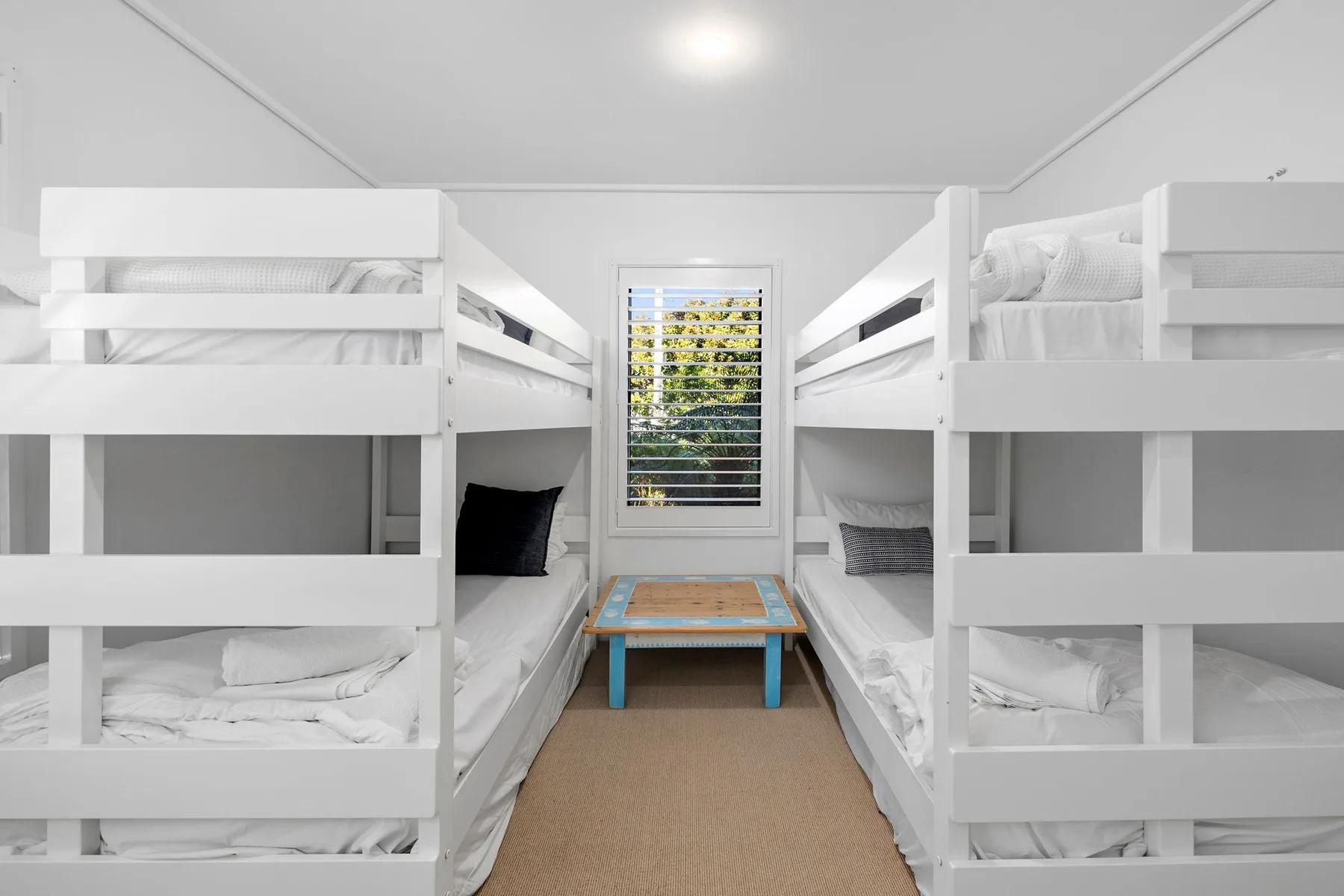 Un dormitorio con literas blancas y una mesa pequeña junto a la ventana.