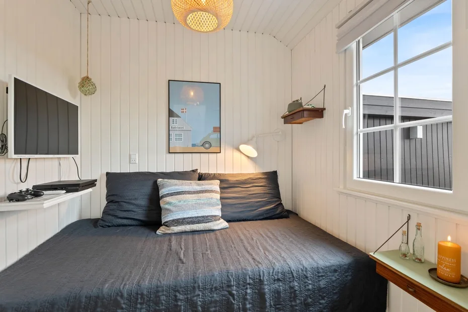 Dormitorio con una cama grande, un televisor en la pared y una ventana luminosa.