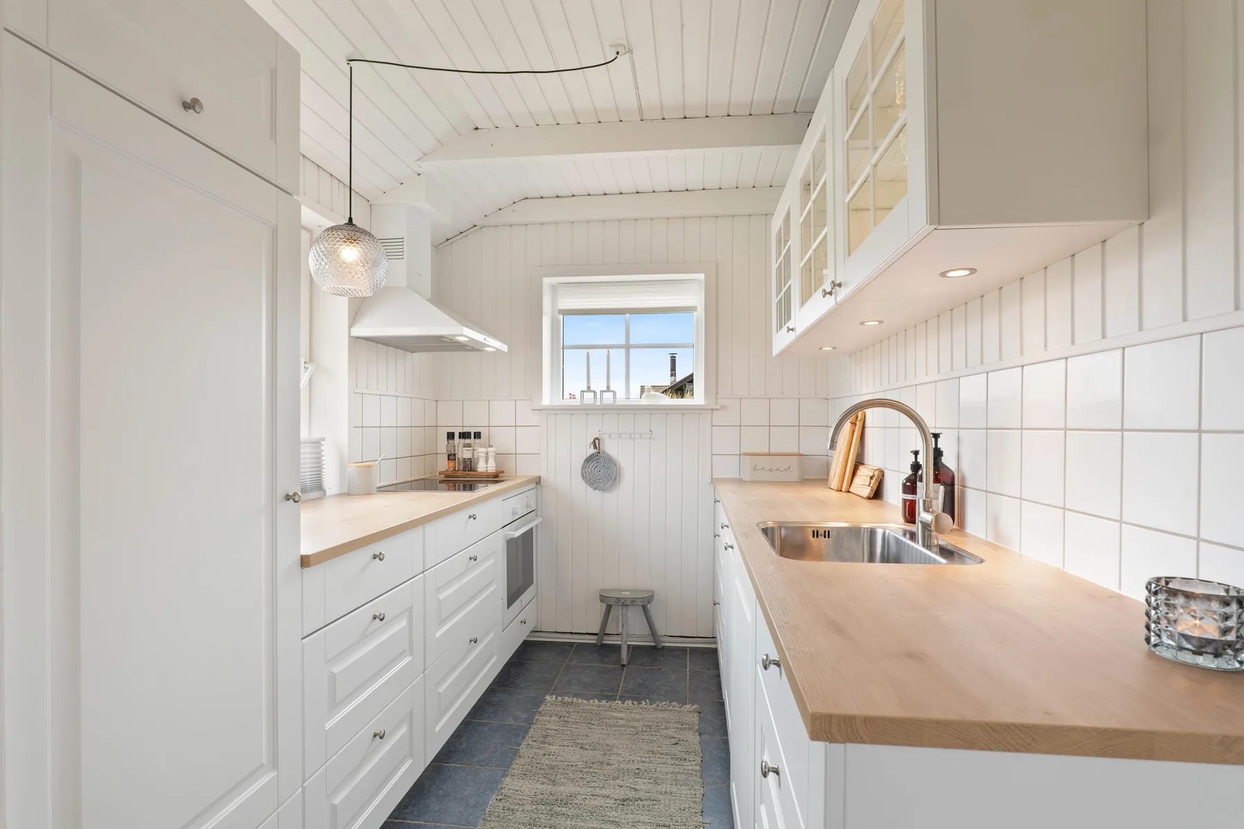Una cocina blanca y luminosa, con encimeras de madera y una ventana al fondo.